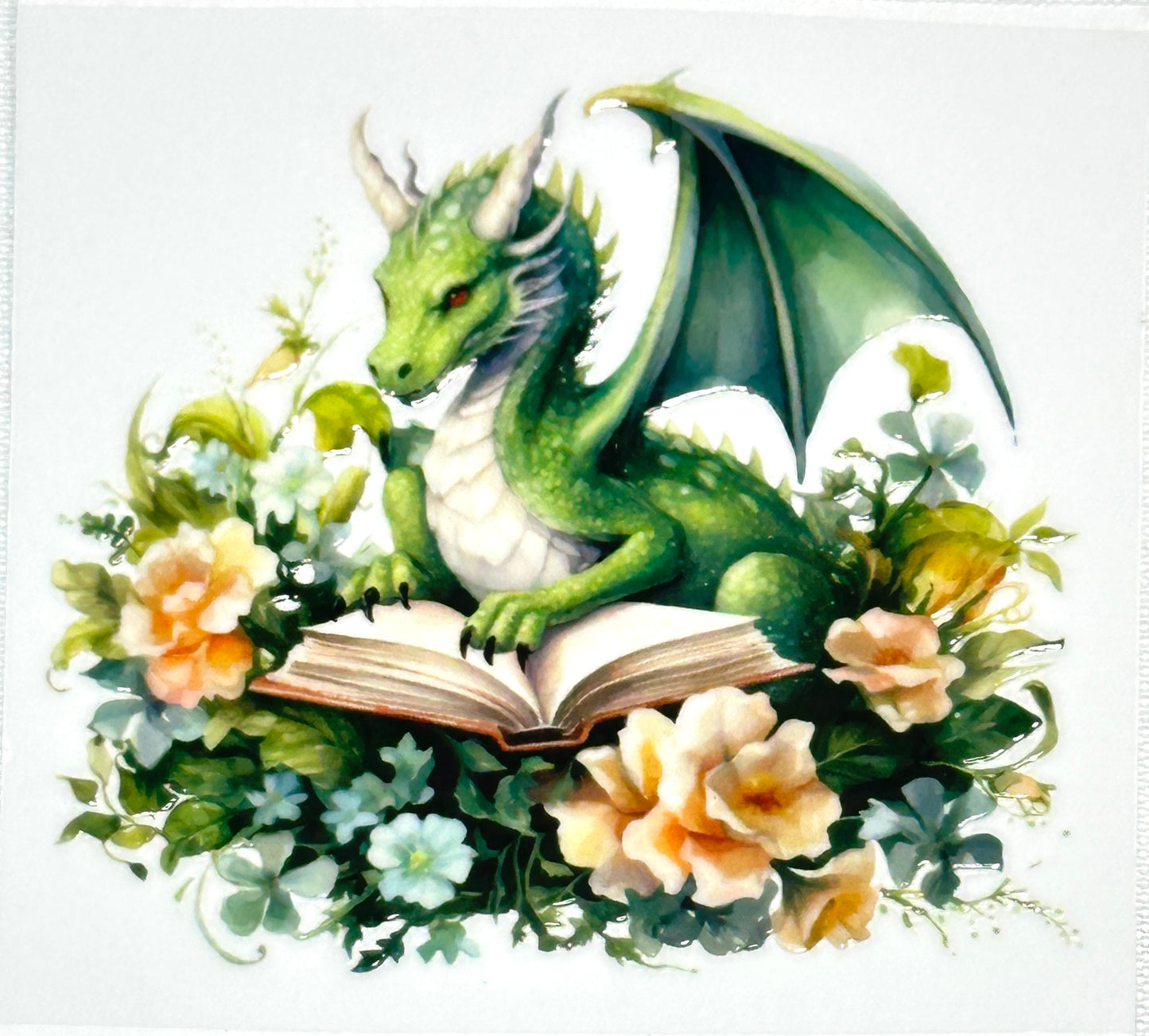 Green dragon reading a book surrounded by flowers on a white background
