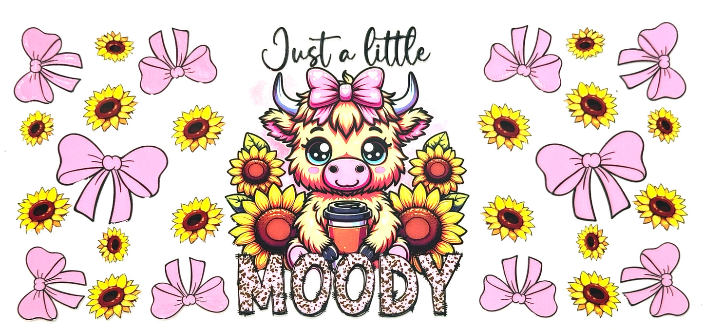 Cartoon cow with a coffee cup surrounded by sunflowers and pink bows with text 'Just a little MOODY'.