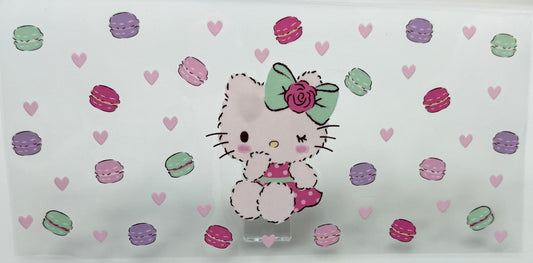 HK character with a green bow on a colorful macaron and heart patterns.