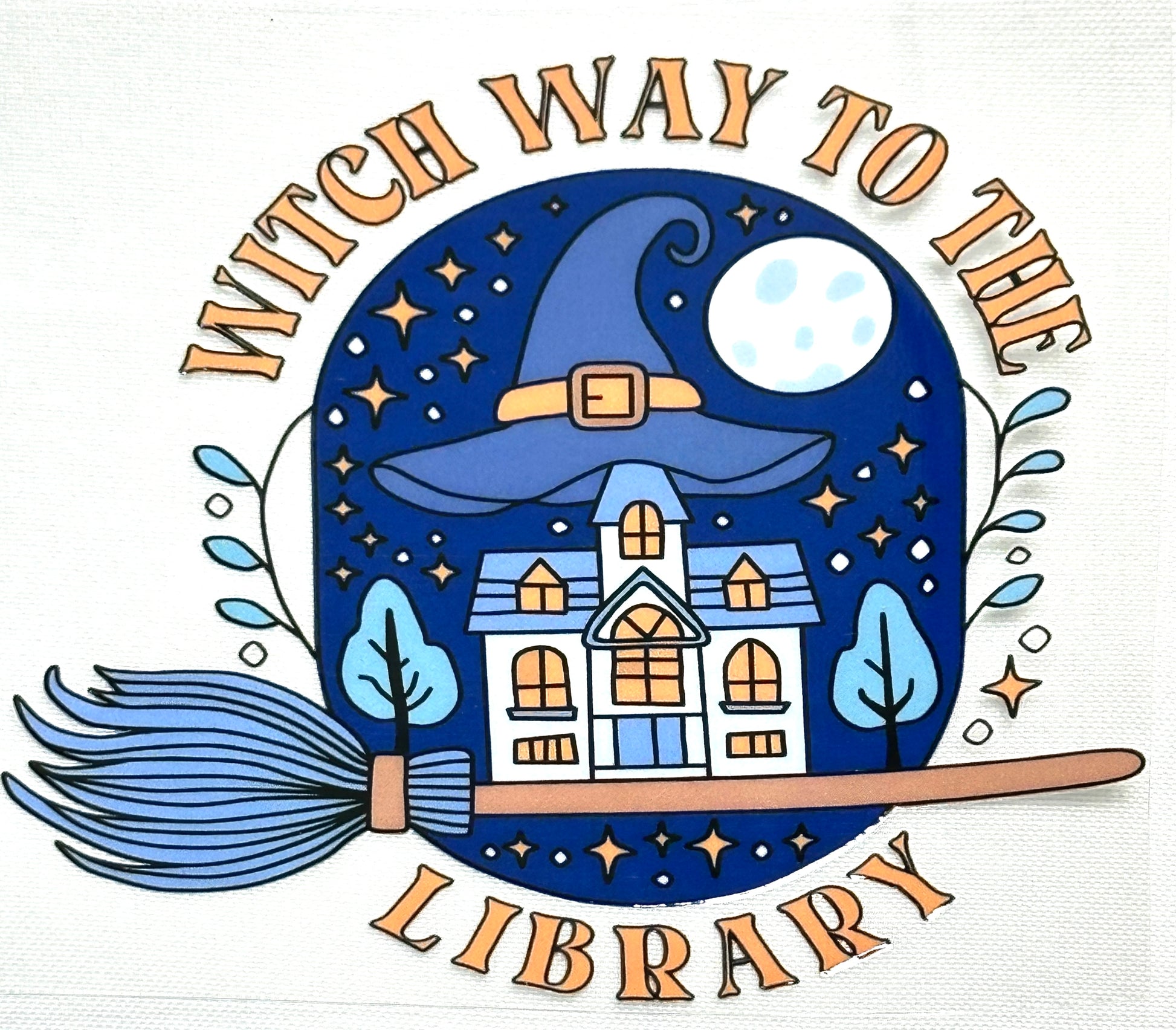 Illustration of a witch's hat with a house inside, surrounded by trees and a broomstick, with text 'Witch Way to the Library' on a white background.